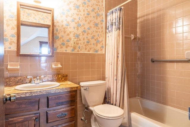 bathroom with tile walls, toilet, wainscoting, vanity, and wallpapered walls