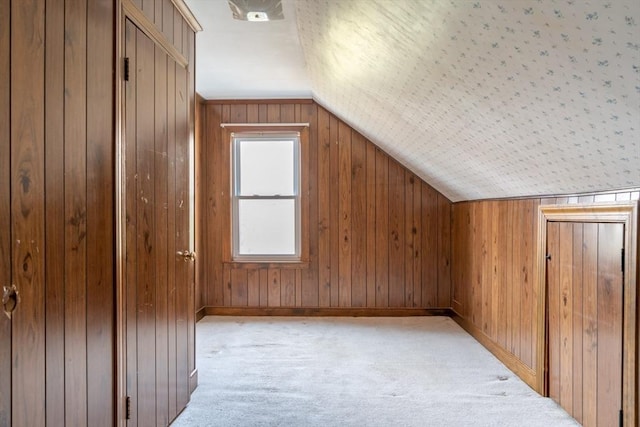 bonus room with lofted ceiling, wood walls, baseboards, and light colored carpet