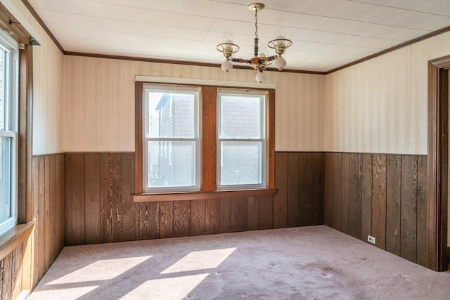 carpeted empty room with a chandelier, wainscoting, ornamental molding, and wood walls