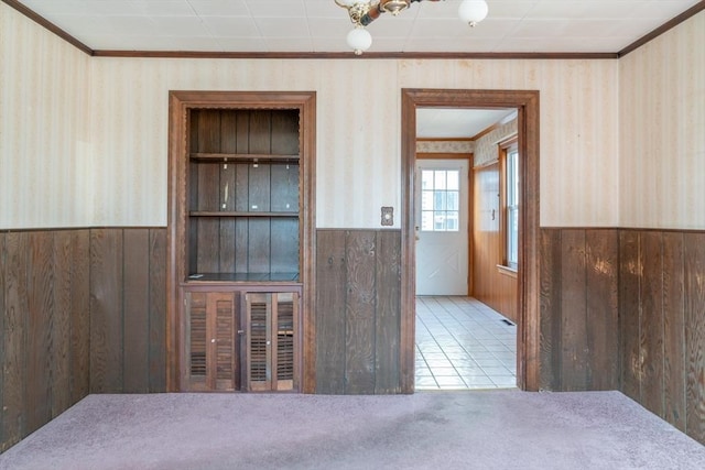 carpeted spare room featuring a wainscoted wall, crown molding, wallpapered walls, and wood walls