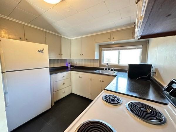 91 W Main St, West Brookfield, MA 01585 - kitchen with cream cabinets, dark countertops, a sink, and white appliances