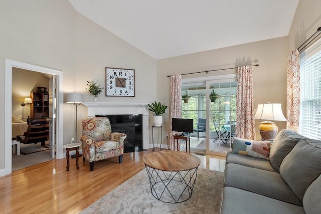 living area featuring light wood-style floors, high vaulted ceiling, and a tiled fireplace