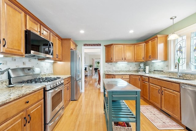 kitchen with stainless steel appliances, a sink, light wood-style flooring, backsplash, and light stone countertops