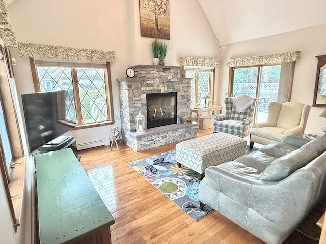 living room featuring a stone fireplace, a wealth of natural light, hardwood / wood-style flooring, and a baseboard heating unit