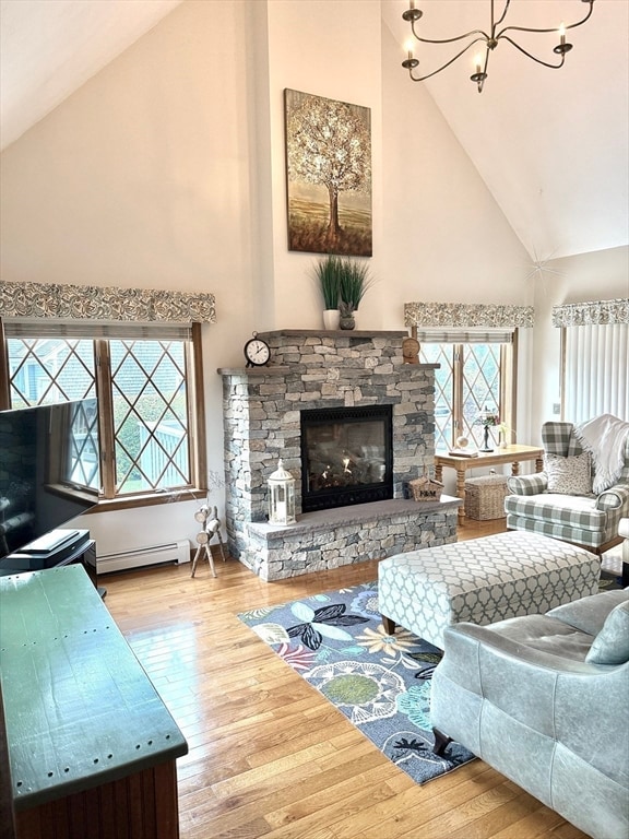 living room with a stone fireplace, a baseboard radiator, a wealth of natural light, hardwood / wood-style flooring, and high vaulted ceiling