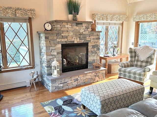 living room featuring a stone fireplace, wood-type flooring, and a baseboard heating unit