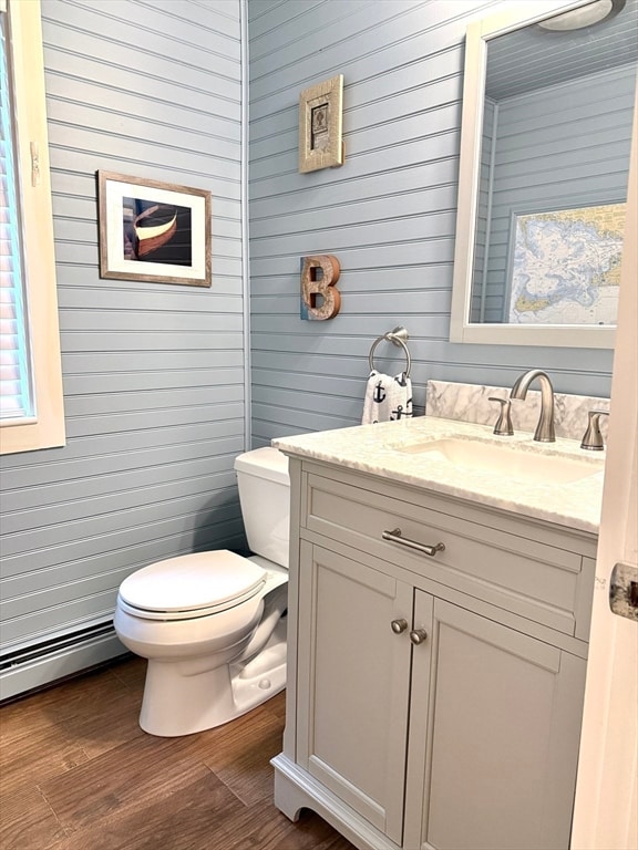 bathroom featuring wood-type flooring, wooden walls, toilet, and vanity