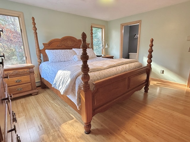 bedroom with light hardwood / wood-style floors, multiple windows, and a baseboard heating unit