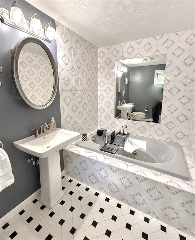 bathroom with a textured ceiling, tiled tub, toilet, and sink