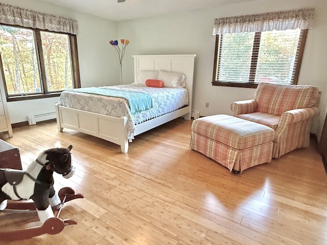 bedroom with multiple windows, baseboard heating, and light hardwood / wood-style flooring