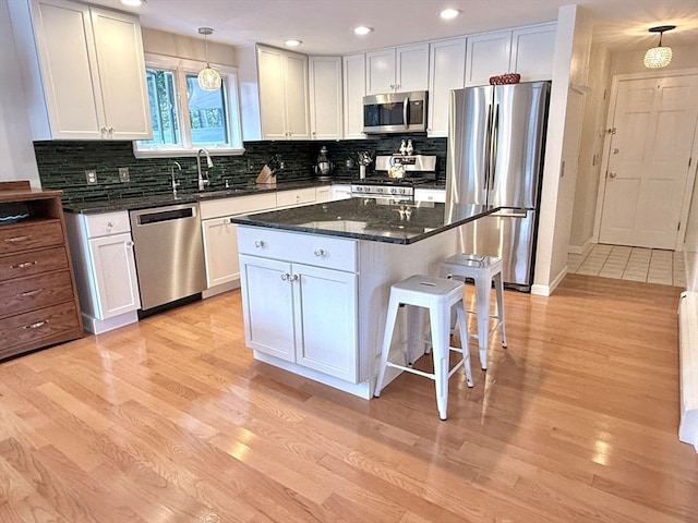 kitchen with white cabinets, light wood-type flooring, appliances with stainless steel finishes, and pendant lighting