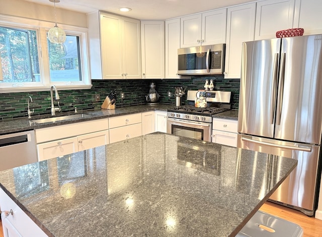 kitchen featuring stainless steel appliances, sink, tasteful backsplash, white cabinetry, and dark stone countertops