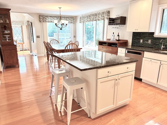 kitchen with backsplash, decorative light fixtures, a kitchen island, light wood-type flooring, and dishwasher