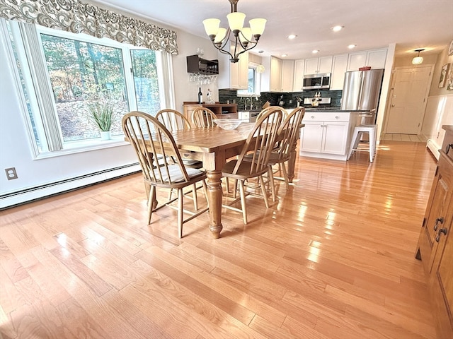 dining area featuring light wood-type flooring, sink, a notable chandelier, and a baseboard radiator