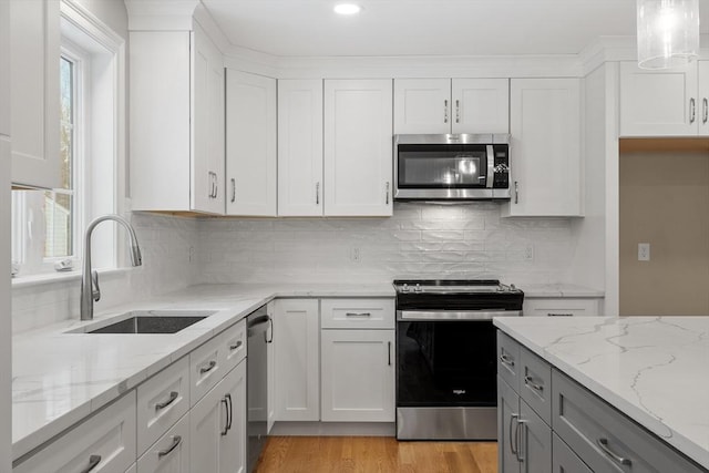 kitchen with sink, white cabinets, light stone counters, stainless steel appliances, and light hardwood / wood-style flooring