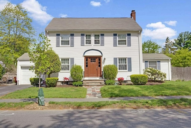 colonial-style house with a chimney, asphalt driveway, and a garage