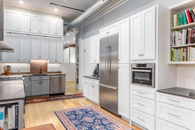 kitchen with dark countertops, white cabinets, a sink, light wood-style flooring, and appliances with stainless steel finishes