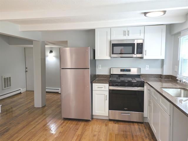3 S Shore Rd, Salem, NH 03079 - kitchen with appliances with stainless steel finishes, a baseboard radiator, white cabinetry, light wood-type flooring, and beam ceiling