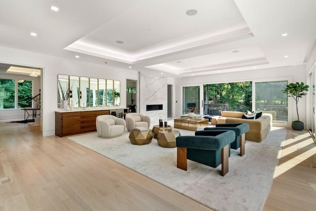 living room with a high end fireplace, a tray ceiling, and light wood-type flooring