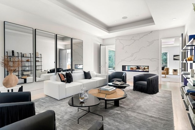 living room featuring a high end fireplace, a raised ceiling, and light wood-type flooring