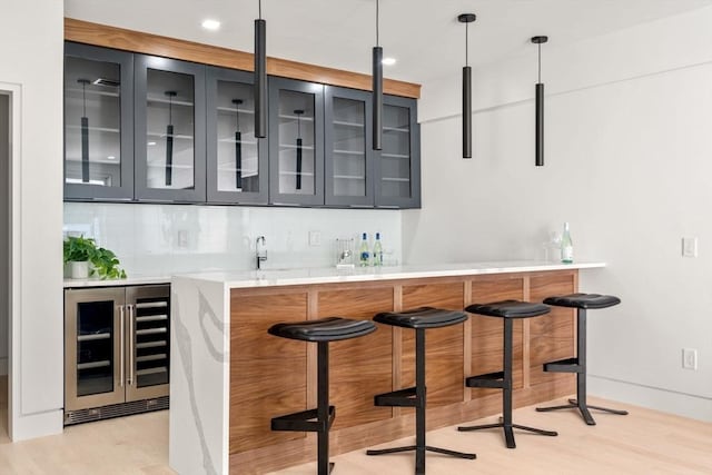 bar featuring pendant lighting, backsplash, light hardwood / wood-style floors, and beverage cooler