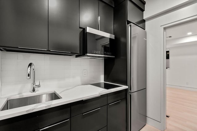 kitchen featuring sink, black appliances, light wood-type flooring, light stone countertops, and backsplash