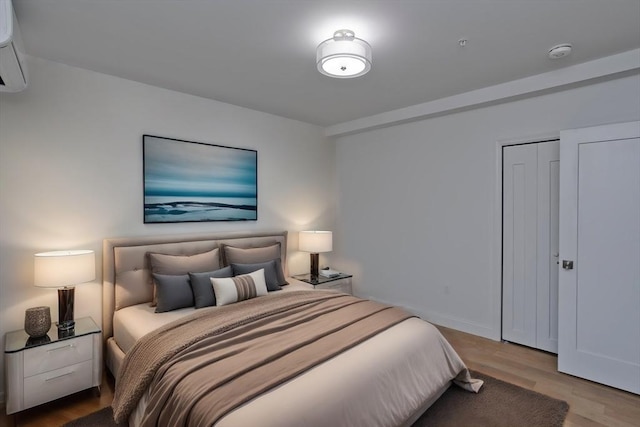 bedroom with a closet, a wall mounted air conditioner, and light hardwood / wood-style flooring