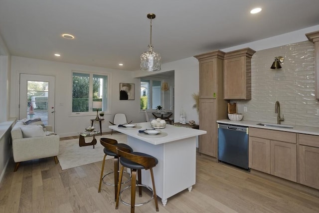 kitchen with sink, hanging light fixtures, a kitchen breakfast bar, light hardwood / wood-style floors, and stainless steel dishwasher