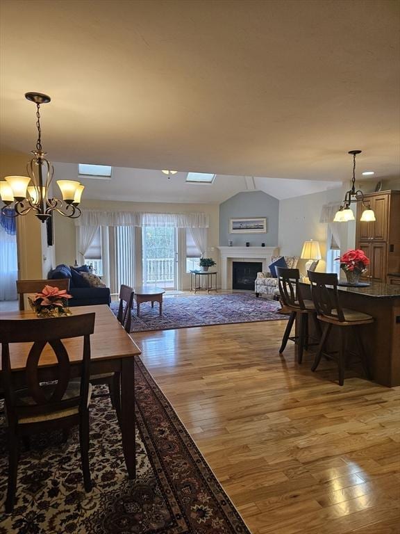 dining space with wood-type flooring, lofted ceiling with skylight, and a chandelier