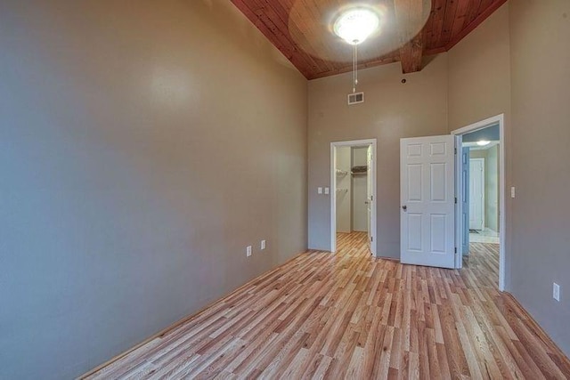 empty room with beam ceiling, a towering ceiling, wood ceiling, and light hardwood / wood-style flooring