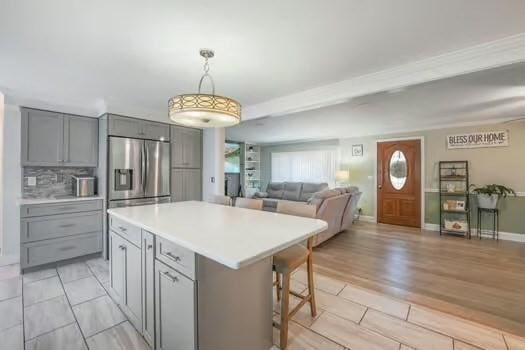 kitchen with a breakfast bar, gray cabinetry, hanging light fixtures, stainless steel fridge, and a kitchen island