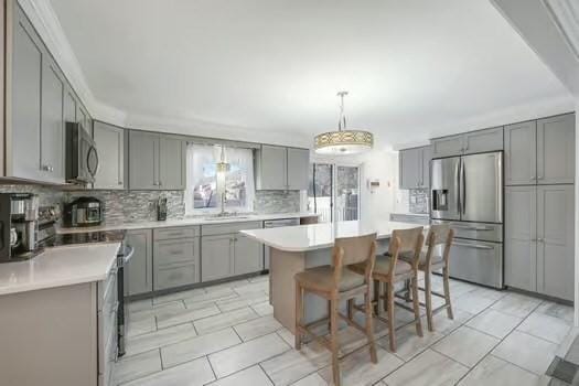 kitchen with a kitchen island, appliances with stainless steel finishes, gray cabinetry, and decorative light fixtures