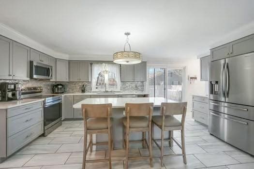 kitchen featuring gray cabinetry, backsplash, stainless steel appliances, a center island, and decorative light fixtures