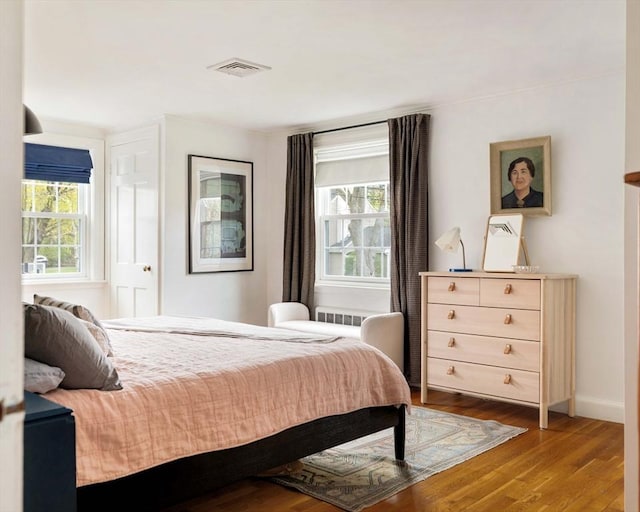 bedroom with baseboards, multiple windows, visible vents, and wood finished floors