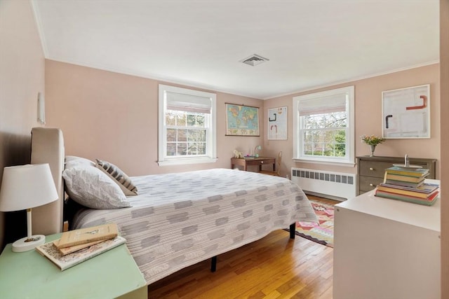 bedroom featuring radiator, crown molding, visible vents, and wood finished floors