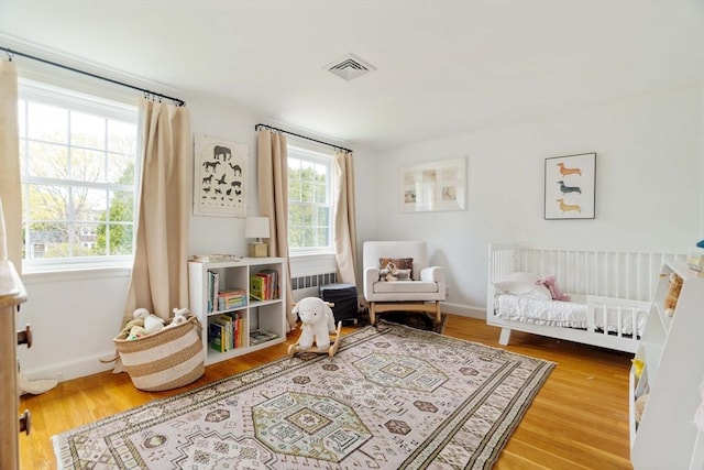 bedroom featuring a crib, visible vents, wood finished floors, and baseboards