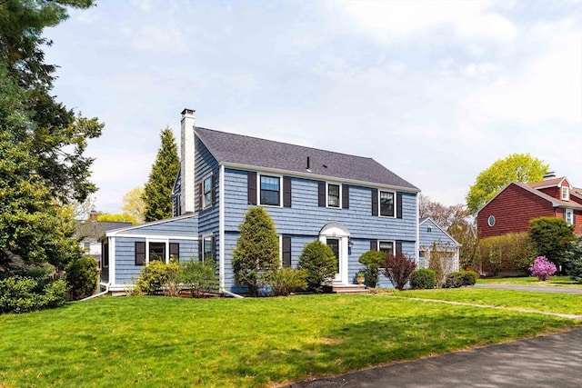 colonial-style house featuring a chimney and a front lawn