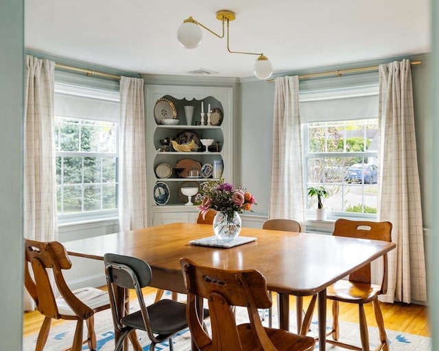 dining space with light wood finished floors, ornamental molding, plenty of natural light, and visible vents
