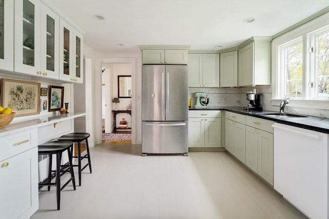 kitchen featuring glass insert cabinets, a sink, freestanding refrigerator, backsplash, and dishwasher