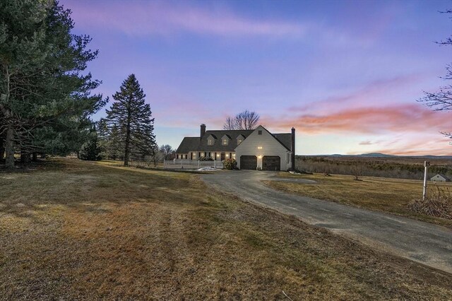 view of front facade with a yard, driveway, a chimney, and a garage