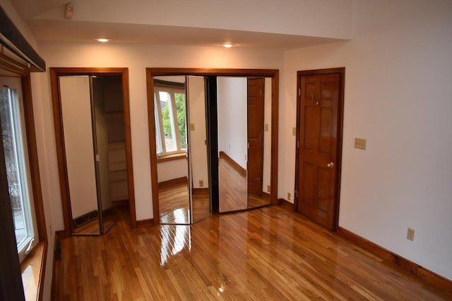 unfurnished bedroom with wood-type flooring and multiple closets