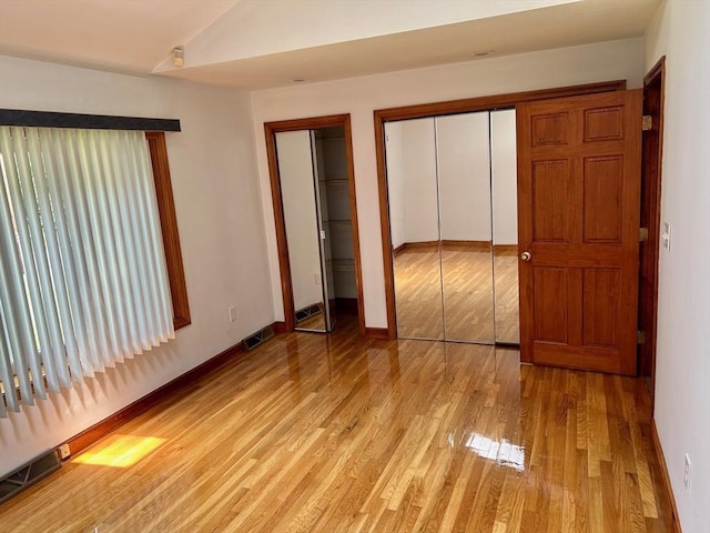 unfurnished bedroom featuring multiple closets, lofted ceiling, and light wood-type flooring