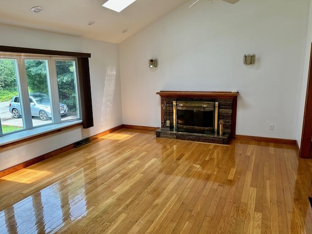 unfurnished living room featuring a fireplace, lofted ceiling with skylight, light hardwood / wood-style flooring, and ceiling fan