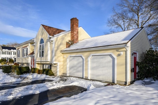 snow covered property with an attached garage and a chimney