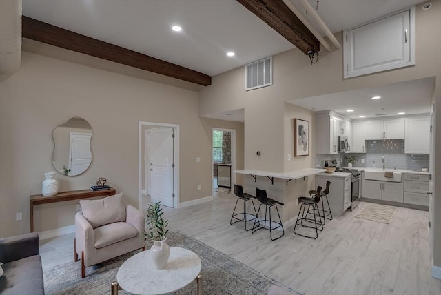 kitchen featuring a breakfast bar, stainless steel appliances, beam ceiling, light hardwood / wood-style flooring, and white cabinets