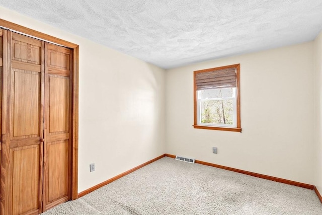 unfurnished bedroom featuring visible vents, a textured ceiling, baseboards, and carpet flooring