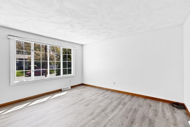 empty room featuring a textured ceiling, baseboards, visible vents, and wood finished floors