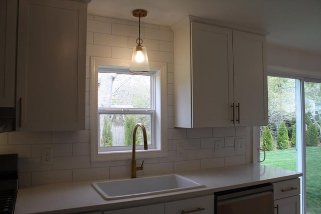 kitchen featuring a sink, dishwasher, light countertops, decorative light fixtures, and tasteful backsplash