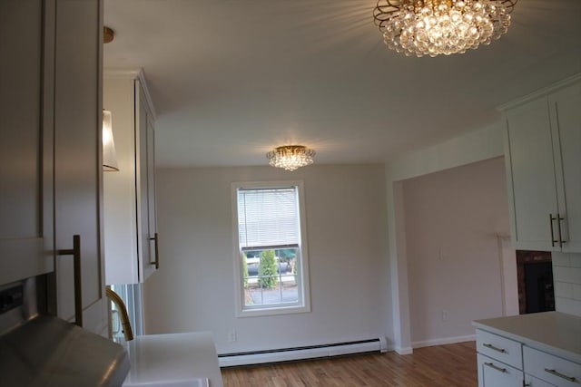 kitchen with wood finished floors, light countertops, a baseboard heating unit, a notable chandelier, and white cabinetry