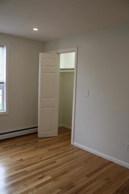 unfurnished bedroom with baseboards, baseboard heating, a closet, and light wood-type flooring